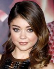 Sarah Hyland with her long side parted hair styled into loose curls