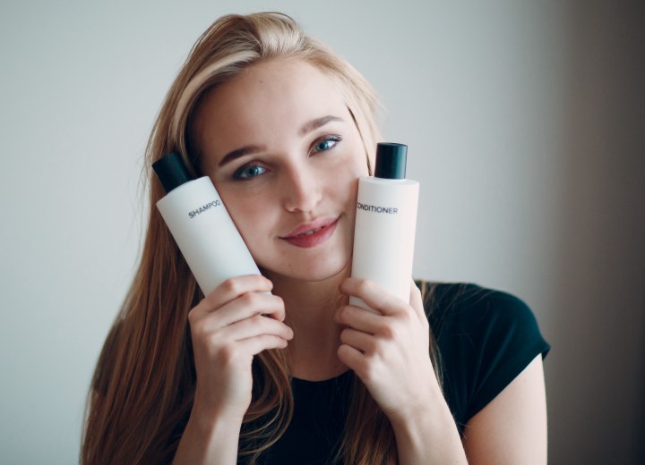 Young woman holding bottles with shampoo and conditioner