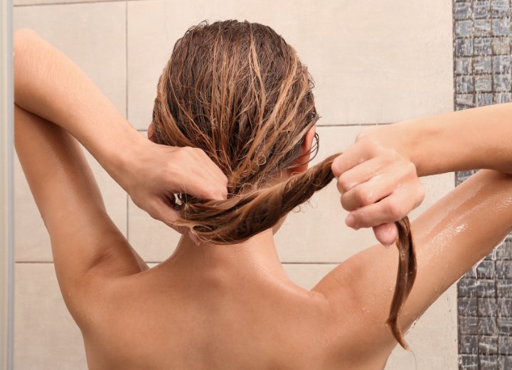 Woman while rinsing out her long hair with warm water