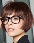 Short layered brunette bob with wispy bangs and paired with eyeglasses