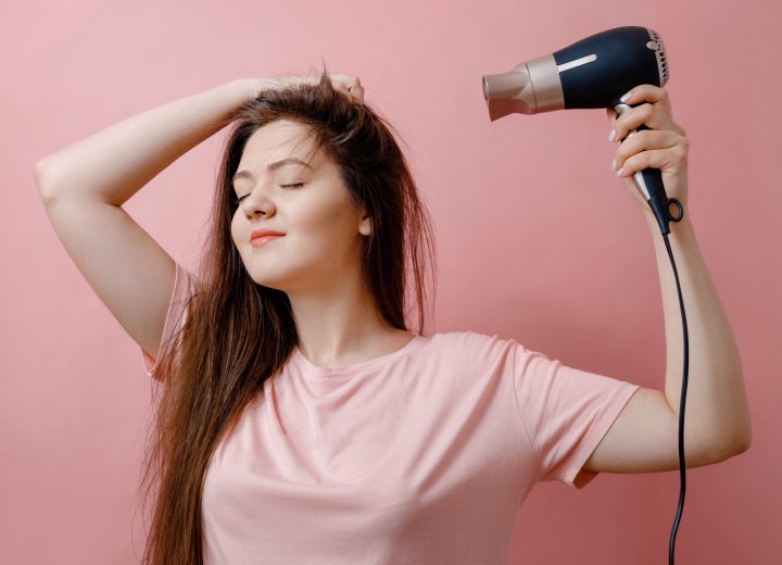 Young woman who is blow drying her hair, using a blow dryer with a regular nozzle