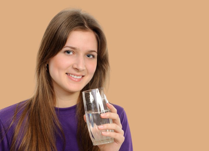 Girl with healthy long hair and drinking a glass of water