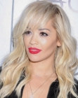 Rita Ora sporting long blonde hair with bangs, loose waves and curls