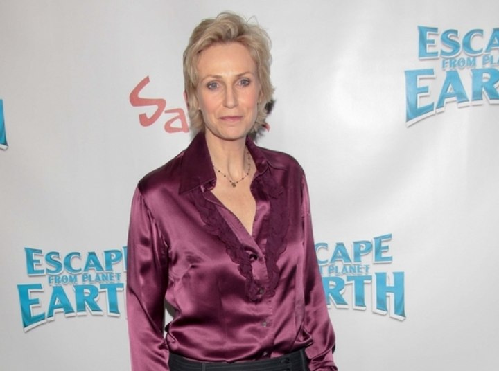 Jane Lynch wearing a purple silk blouse and trousers