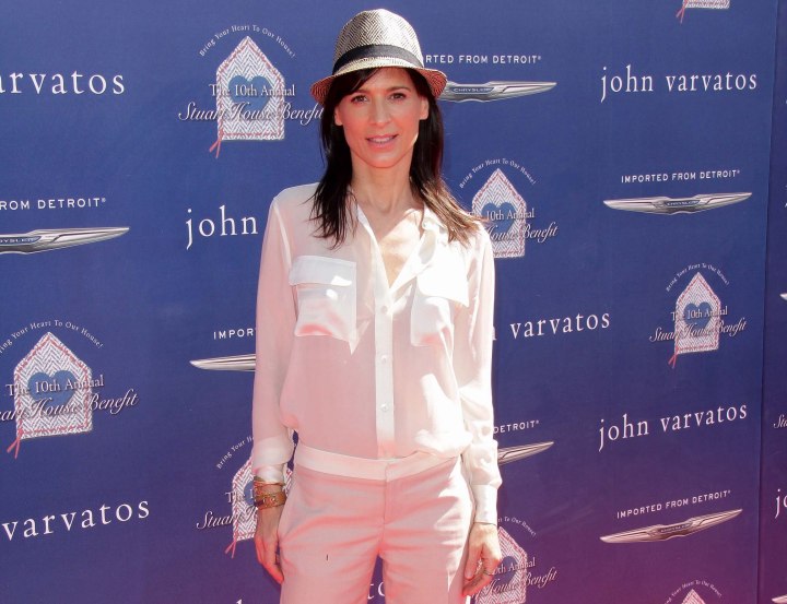 Perrey Reeves wearing a sheer shirt, white trousers and hat