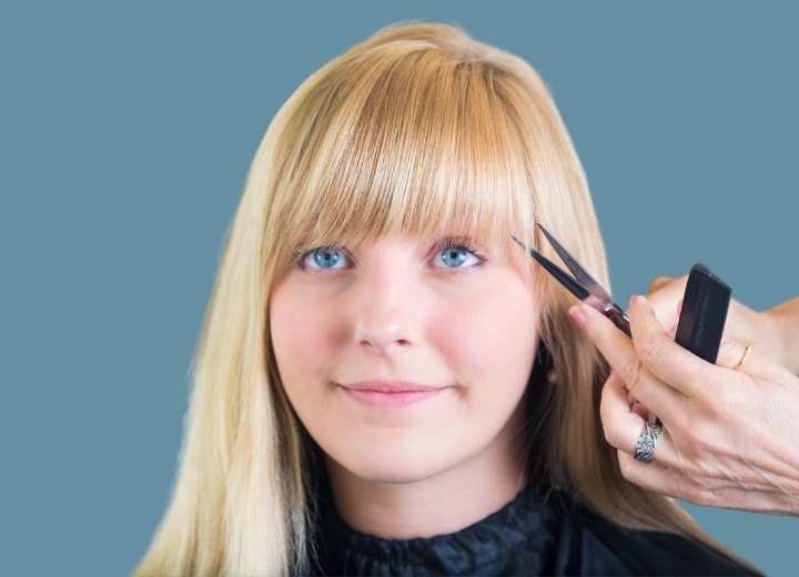 Coiffeur taillant la frange d'une cliente heureuse dans un salon de coiffure