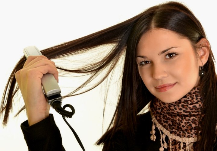 Brunette girl who is straightening her long hair with a flat iron