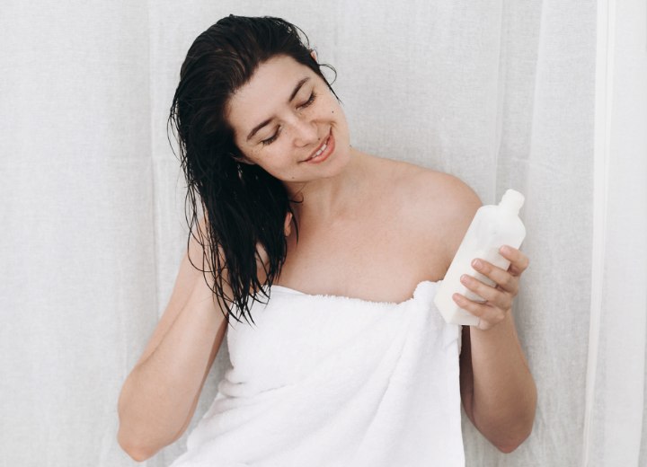 Woman with wet hair checking out a bottle with conditioner