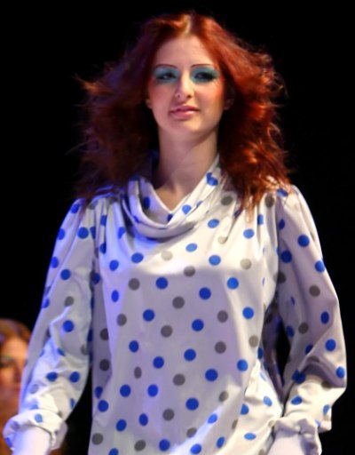 Model with red curly hair wearing a silky cowl neck top with polka dots