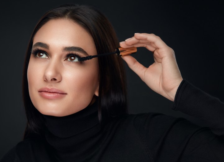 Woman wearing a turtleneck and applying mascara