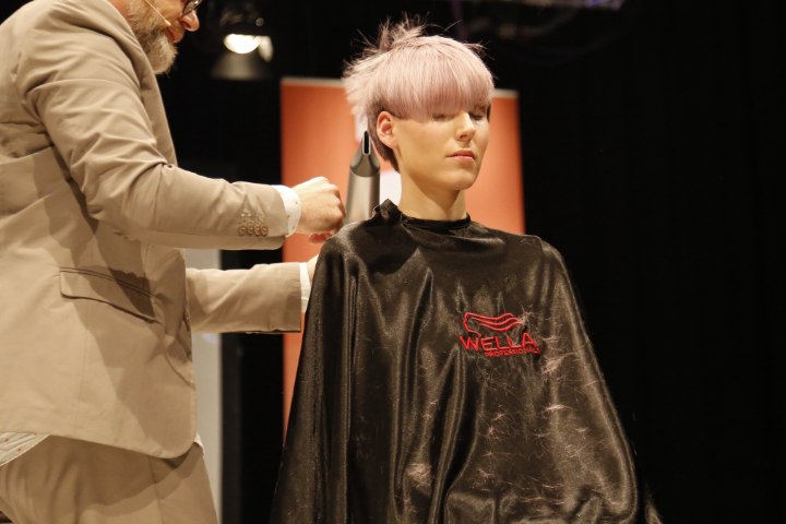 Hair model with her finished short hairstyle and still wearing her shiny hair cutting cape