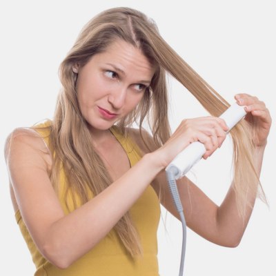 Woman whos is styling her hair with a flat iron